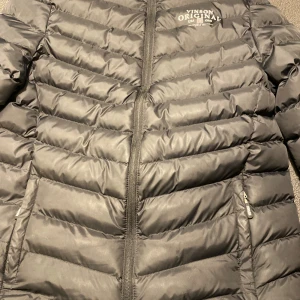 Svart pufferjacka från Vinson Original - Säljer en svart pufferjacka från Vinson Original med tryck på bröstet och siffran 23 på ena ärmen. Jackan har dragkedja framtill och två sidofickor med dragkedja. Perfekt för kalla dagar och har en sportig vibe.