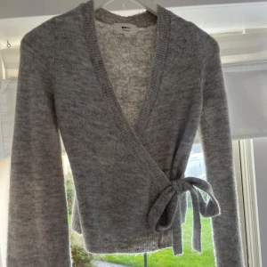 Grå omlottkofta från Gina Tricot -  grå omlottkofta från Gina Tricot med knyt i sidan. Koftan är stickad, har lång ärm och v-ringning. Använd ca 2 gånger! 