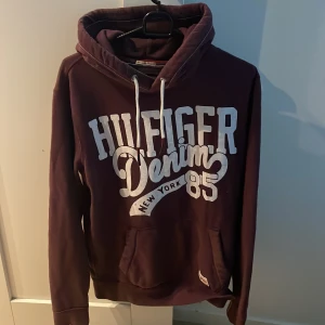 Vinröd hoodie Hilfiger Denim - Säljer en vinröd hoodie från Hilfiger Denim i storlek M, modellen är ca 180cm lång, hör av dig vid funderingar!