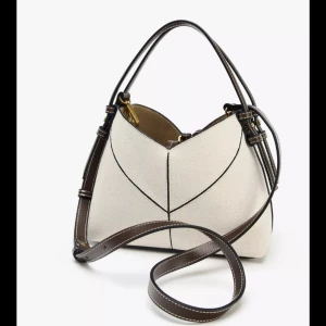 Axelväska Zara - Snygg axelväska från  Zara i vit canvas med bruna skinn-detaljer och svarta kontrastsömmar. Väskan har både handtag och justerbar axelrem, samt guldfärgade metalldetaljer. Perfekt storlek för det viktigaste och ger en clean, modern look. OANVÄND!! 