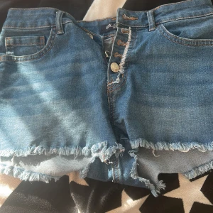 Blå jeansshorts med fransad kant LCW Jeans - Snygga blå jeansshorts från LCW Jeans i klassisk femficksmodell. Shortsen har fransad och rå kant nedtill, knappgylf och slitna detaljer vid knapparna. Perfekta för sommarens chill dagar och har en normal passform.