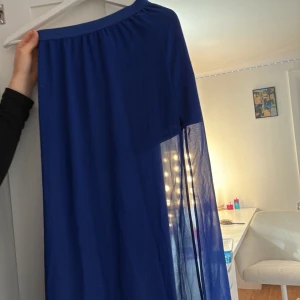 Blå långkjol med transparent detalj - Snygg blå långkjol med bred resår i midjan och en cool transparent panel nertill. Kjolen har en flowy känsla och är perfekt för dig som gillar att sticka ut lite extra. Materialet är lätt och ger ett luftigt intryck.