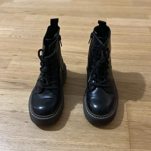 Svarta boots från H&M med snörning - Svarta boots från H&M med chunky sula, snörning framtill och dragkedja på sidan för enkel påtagning. Skorna är i syntetmaterial med rund tå och grov yttersula som ger en cool look. Perfekta för dig som gillar en edgy stil.