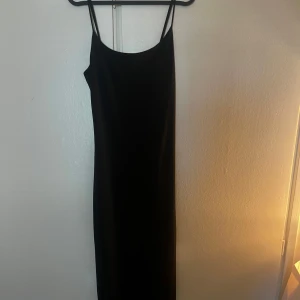 Svart långklänning med smala axelband - Säljer en stilren svart långklänning med smala axelband och rak siluett. Klänningen har en enkel och elegant design som ger en snygg look. Perfekt för dig som gillar minimalistisk stil och vill ha en klänning som är lätt att matcha med accessoarer.
