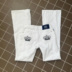 Victoria Beckham jeans - Så snygga vita låga jeans från Victoria Beckham med utsvängda ben och svarta kronor på fickorna. Jeansen är något missfärgade nertill (se sista två bilderna) eftersom de varit allt för långa på mig men i övrigt i mycket fint skick. Innerbenslängd är 84 cm, midja rakt över 37 cm och midjehöjd 19,5 cm. Använd köp nu🫶🏼