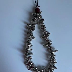 Silvrigt mobilarmband med chunky pärlor - Unikt mobilarmband med chunky, oregelbundna pärlor i silverfärg och en röd detalj vid fästet. Perfekt att hänga på mobilen för en cool och trendig look. Armbandet har en glansig finish och ger riktigt statement-vibes.