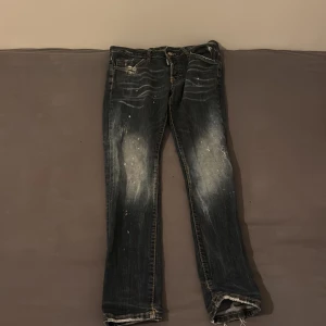 Svarta Dsquared2 jeans med slitningar - Snygga svarta jeans från Dsquared2 med slitna detaljer och ljusa partier framtill. Jeansen har en rak passform, klassiska fickor och coola slitningar vid bensluten. Perfekta för dig som gillar en edgy streetstil. Har en liten söndrig fika inuti byxan passar storleken xs och s 