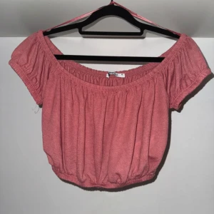 Korallfärgad offshoulder topp från Gina Tricot - Söt korallfärgad offshoulder topp från Gina Tricot med korta ärmar och resår både upptill och nertill. Modellen är croppad och har en luftig, rynkad design som ger en avslappnad vibe.