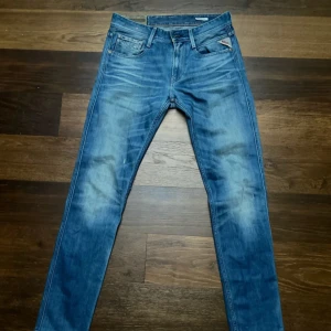 Replay Anbass blå jeans herr - Snygga blå Replay Anbass jeans med klassisk femficksdesign och diskreta slitningar. Jeansen har smal passform och normal midja, med Replay-logga på fickan och bak på linningen. Perfekta för dig som gillar en modern och stilren look.    Längden: 105cm.   Bredd: 41cm   Vid frågor eller funderingar är det bara att höra av sig! 
