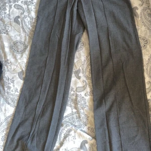 Grå kostymbyxor från Pull&Bear XS - Snygga grå kostymbyxor från Pull&Bear i storlek XS. Byxorna har raka ben, klassisk passform och stängs med knapp och dragkedja. Perfekta för en clean och stilren look. Materialet känns mjukt och lätt, vilket gör dem bekväma hela dagen.