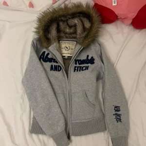 !!Reserverad!! Abercrombie & Fitch hoodie - Grå hoodie med päls på insidan samt luvkanterna från äldre A&F med logga fram. Strl ”XL” men det stämmer inte, passar som en S. Inga defekter! Skriv om ni är intresserade/har frågor 🫶