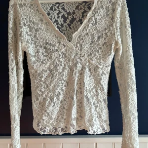 Vit spetsblus från Gina Tricot - Säljer en superfin vit spetsblus från Gina Tricot i storlek M. Blusen har lång ärm, v-ringning och är helt täckt av blommig spets. Perfekt att styla med jeans eller kjol för en romantisk look.