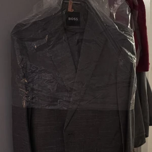 Grå kavaj från BOSS - Säljer en stilren grå kavaj från BOSS med klassisk passform och snyggt snitt. Perfekt för dig som vill ha en tidlös och elegant look. Kavajen har diskreta knappar framtill och är tillverkad i ett mjukt material som känns lyxigt. Byxorna kommer med också i nytt skick 