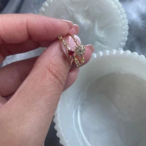 Två guldiga ringar med stenar / 18 k guldpläterade ringar  - Säljer två tunna guldiga ringar, en med en röd hjärtformad sten och små klara stenar, och en med en stjärnformad detalj med gnistrande stenar.  Köpta i tyurkiet! Perfekta att bära tillsammans eller var för sig för en söt och trendig look. Storlek 7 som är storlek 15 