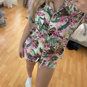 Blommig satinpjamas set  Victoria's Secret S-XS - Säljer ett  blommigt pyjamas set från Victoria’s Secret i storlek XS-S. De har en vit bas med gröna och rosa blommor, tröjan är som ett skjort material med vita knappar där fram och en ficka vid bröstet och nervikt krage 