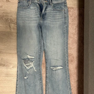 Blå bootcut jeans med slitningar - Snygga blå bootcut jeans i relaxed fit med slitna detaljer och hål på benen. Jeansen har midwaist och klassisk femficksdesign. Perfekta för dig som gillar en avslappnad och trendig look. Helt nya endast provade men kan inte skicka tillbaka pågrund av lappen är borta 