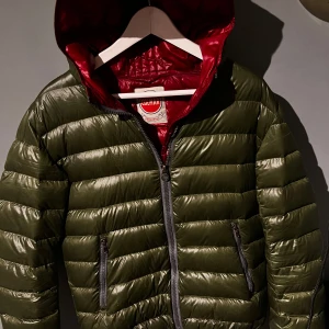 Olivgrön dunjacka från Colmar - Schysst olivgrön dunjacka från Colmar med huva och röda detaljer på insidan. Jackan har en snygg design, dragkedja framtill och två sidofickor med dragkedja. Perfekt nu är kylan kommer. Passar perfekt till de flesta stilar. Om du är intresserad eller har minsta lilla fundering så tveka inte på att höra av dig. Kan tänka mig att gå ner i pris vid en snabb och smidig affär🤝
