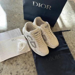 Di0r B30 vita sneakers - Säljer ett par fina vita Di0r B30s med tydliga CD-loggor på sidorna och hälen i storlek 44. Skorna är i använt skick men dom har fortfarande mycket att ge! Påse, dustbag och extra snören ingår och allt fraktas inom 24h✅ Hör gärna av er vid frågor🏌️