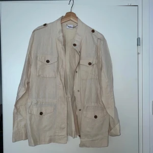 Beige höstig  tunnjacka från  Saint Tropez - Stilren beige tunnjacka  från Saint Tropez i linneblandning. Jackan har fyra fickor framtill med knappar, axelklaffar och snörning ( snöret har löst upp sig lite )  i midjan för en snygg passform. Perfekt lager-på-lager-plagg med avslappnad vibe och snygga detaljer.