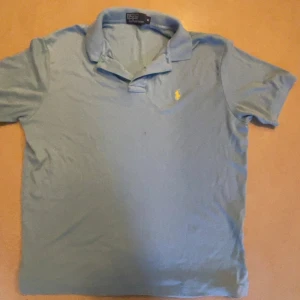 Ljusblå Polo t-shirt från Ralph Lauren - Snygg ljusblå t-shirt från Polo Ralph Lauren med klassisk krage och korta ärmar. Ikoniska gula loggan broderad på bröstet. Perfekt för dig som gillar stilrena och tidlösa plagg. Mjuk bomull som känns skön mot huden.