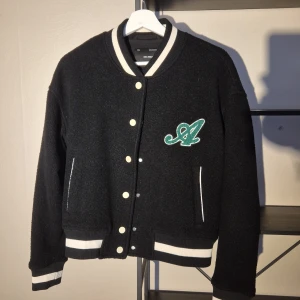 Axel Arigato Black College bomber jacket  - Black college bomber jacket from Axel Arigato with white-striped cuffs and collar. The jacket features an embroidered green logo on the chest and large “Axel Arigato” embroidered lettering on the back. It closes with front buttons and has two pockets. The material is a wool blend that gives it a nice texture. Completely unworn :)    
