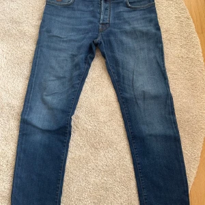 Jacob Cohen blå jeans med orange detaljer - Snygga blå jeans från Jacob Cohen med klassisk femficksdesign och orange kontrastsömmar. Jeansen har en unik gul patch med logotyp bak och broderad J på myntfickan. Tillverkade i mjukt jeansmaterial med smal passform och exklusiv känsla. Passar w33 eller w32