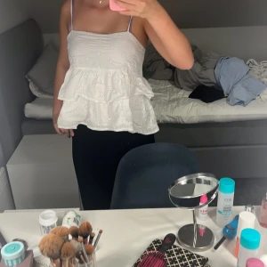 Vit volangig linnetopp med broderi - Supersöt vit linnetopp med tunna axelband och broderade detaljer. Toppen har två lager volanger som ger en romantisk och luftig känsla. Perfekt för varma dagar och enkel att matcha med både jeans och kjol.