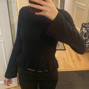 Svart volangtröja från Gina Tricot - Supersöt svart långärmad tröja från Gina Tricot med smockad kropp och volangkant nedtill. Passformen är 154/164. Den säljs pga att jag har för många svarta tröjor 🤗🖤