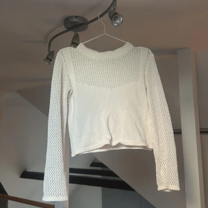Vit stickad tröja från Zara - Snygg vit stickad tröja från Zara med långärmade meshdetaljer och ribbad krage. Tröjan har ett coolt hålmönster på ärmar och upptill, vilket ger en fräsch och trendig look. Perfekt att styla med jeans eller kjol för en chill vibe.