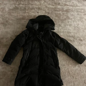 Svart lång dunjacka med huva - Säljer en svart lång canada goose (shelburne) jackan är i bra skick. Utöver att en knapp har blivit lite konstigt, men inget man märker av man kan byta den i värsta fall därav priset. Storlek xxl men eftersom att det är en fusion fit model sitter den mer som en Xl/L.