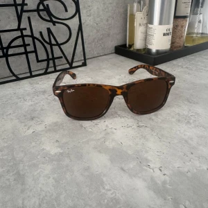 Ray-Ban  leopardmönstrade solglasögon - Snygga Ray-Ban Wayfarer solglasögon med leopardmönstrad båge i bruna och svarta toner. Klassisk fyrkantig form och mörka glas. Perfekt accessoar för att lyfta din stil med en cool och tidlös vibe.
