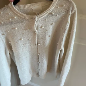 Pärlprydd kofta från H&M i beige - Superfin beige kofta från H&M med pärldetaljer på framsidan. Koftan har rund halsringning, knappar framtill och är långärmad. Perfekt för dig som gillar en söt och stilren look med det lilla extra.