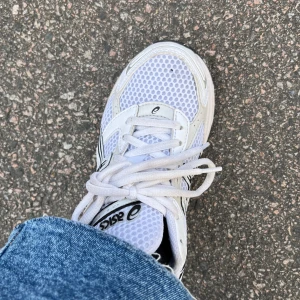 Vita Asics Gel-1130 sneakers - Säljer ett par vita Asics Gel-1130 sneakers med mesh- och syntetpaneler, svarta detaljer och klassisk snörning. Skorna har en sportig vibe med rund tå och platt sula, perfekta för dig som gillar retrostil och komfort.