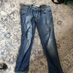 Blå jeans från Jacob Cohen - Snygga blå jeans från Jacob Cohen med klassisk femficksdesign och ljusa slitningar framtill. Jeansen är tillverkade av utvalda japanska tyger och har raka ben samt grönt patch bak i midjan. Perfekt passform och stilren look.