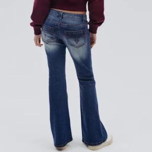 Blå bootcut jeans med röd söm - Snygga blå bootcut jeans med låg midja och röda dekorativa sömmar på bakfickorna. Jeansen har en klassisk femficksmodell och lätt slitning på låren för en cool look. Perfekta för dig som gillar en avslappnad men trendig stil. Använd kanske 5 gånger så ändå nyskick. Nypris 400kr