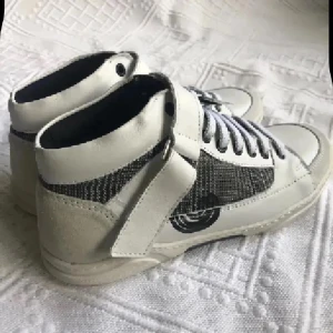 Vita och svarta high top skinn  sneakers NYA - Säljer ett par snygga high top sneakers i vitt och svart med coolt rutigt mönster på sidorna. Skorna har snörning, bred kardborre över vristen och detaljer i mocka och skinn. Perfekta för dig som vill sticka ut med en unik streetstil.