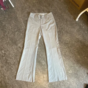 Beiga kostymbyxor  med bootcut - Snygga beiga kostymbyxor med bootcut och hög midja. Byxorna har två knappar framtill och bälteshällor. Perfekta för en stilren och avslappnad look. Lätta och luftiga i materialet, passar grymt till sneakers eller sandaler.