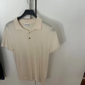 Beige pikétröja från John Henric - Snygg beige pikétröja från John Henric med klassisk krage och två knappar framtill. Tillverkad i mjukt material som känns skönt mot huden. Perfekt för en clean och stilren look.