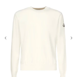 Mörkblå stickad tröja från Moncler - Klassisk fast mörkblå stickad tröja från Moncler med rund halsringning och diskret logga på ärmen. Tröjan har lång ärm och ribbade muddar för en clean och stilren look. Perfekt för dig som gillar minimalistisk stil.