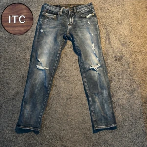 Blå slitna jeans  - Säljer ett par blå jeans med slitningar och hål på benen. Jeansen har klassisk femficksdesign och en snygg tvättad look. 