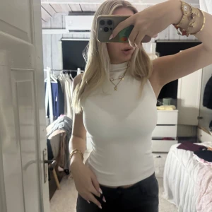 Vit ärmlös polotopp i bomull - Säljer en stilren vit polotopp utan ärmar, i mjukt och stretchigt bomullsmaterial. Toppen har en hög hals och figurnära passform som ger en clean och modern look. Perfekt att matcha med jeans eller kjol för en enkel men snygg outfit.