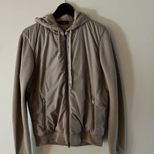 Beige hybridjacka/cardigan från Herno - Snygg och stilren jacka från herno, normal i storleken med något långa ärmar. Säljer den då jag inte hade användning av den. Endast använd ett extremt fåtal gånger