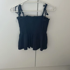 Marinblå smockad linnetopp från SHEIN - Supersöt marinblå linnetopp från SHEIN i storlek XS. Toppen har smockad överdel, volang nertill och knytbara axelband för en justerbar passform. Perfekt till sommaren och enkel att styla med jeans!