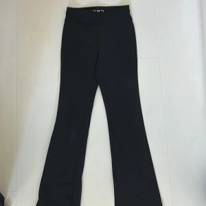 Svarta bootcut träningsbyxor OTP Young 134/140 - Svarta bootcut träningsbyxor från OTP Young i storlek 134/140. Byxorna har snörning i midjan och är tillverkade i ett stretchigt syntetmaterial!