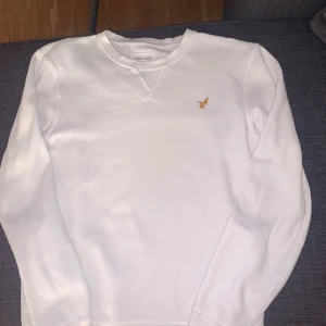 Vit sweatshirt från Pier One - Vit sweatshirt från Pier One med rund hals och broderad guldfärgad fågel på bröstet. Tröjan har långa ärmar och är tillverkad i mjuk bomullsmix som känns skön mot huden. Perfekt för dig som gillar stilrena och enkla plagg med en liten detalj.