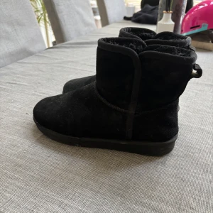 Svarta mockaboots med platt sula - Svarta boots i mocka med rund tå och platt sula. Skorna har en enkel och stilren design med kort skaft och mjukt foder på insidan, perfekta för kyligare dagar. Passar till det mesta och är superbekväma att dra på sig.
