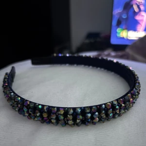 Glittrigt diadem med pärlor - Säljer ett snyggt diadem täckt med små glittrande pärlor i regnbågsfärger. Diademet har en mörkblå bas och pärlorna ger en riktigt cool och glittrig effekt som syns. Perfekt accessoar för att lyfta vilken outfit som helst.