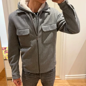 Tjockare grå overshirt  - Stilren grå overshirt med dragkedja, i regular fit. Materialet är mjukt och ulligt, perfekt för lager-på-lager till vintern. Enkel och clean look som passar till det mesta. Finns en liten fläck på ärmen som knappast märks (sista bilden), förutom det är den i mycket bra skick.                                         Skriv vid minsta fundering🤙