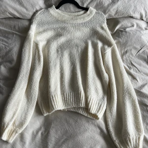 Vit stickad tröja - Mysig vit stickad tröja med rund halsringning. Tröjan har ribbade muddar vid ärmslut och nederkant, vilket ger en snygg och avslappnad look. Perfekt att slänga på sig när det är kyligt ute.