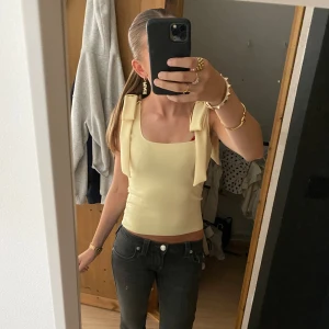 Gul linnetopp med rosettband - Säljer en ljusgul linnetopp med breda axelband som knyts i snygga rosetter på axlarna. Toppen är croppad och har en fyrkantig urringning.